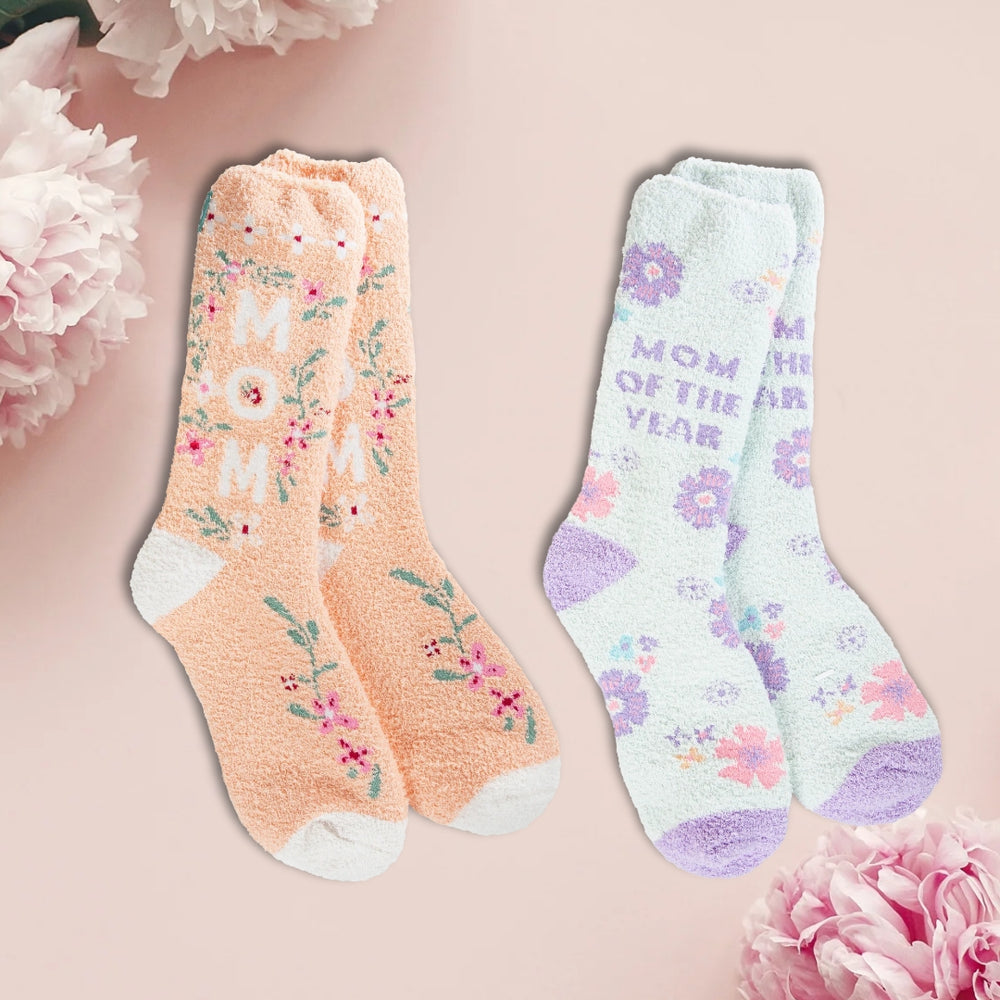 Two pairs of cozy crew socks, one in peach color with blue floral patterns and another in light blue with purple floral patterns, displayed against a pink background with flowers around them.